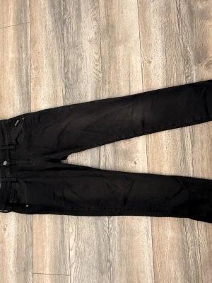 Svarta slim fit jeans - Säljer ett par svarta slim fit jeans med klassisk femficksdesign och bälteshällor. Jeansen har raka ben och diskreta sömmar, perfekta till en avslappnad eller stilren look. Materialet är mjukt och stretchigt för extra komfort.