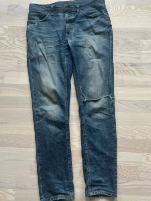 Levi's 511 blå jeans W31 L32 - Säljer ett par klassiska blå Levi's 511 jeans med smal passform och slitningar på benen. Jeansen har fem fickor, dragkedjegylf och är tillverkade i bomull. Perfekta för en avslappnad och trendig look.
