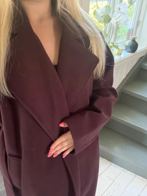Vinröd lång kappa med bred krage - Stilren vinröd kappa med oversized passform och bred krage. Kappan är ifrån New Yorker och går ner till knäna. 