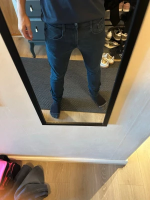 Svarta Replay  slim jeans med fem fickor - Säljer ett par svarta slim fit jeans med klassisk femficksdesign och knappgylf. Jeansen har en smal passform och sitter snyggt längs benen. Perfekta för dig som gillar en stilren och enkel look till vardags. Längden är (34L)
