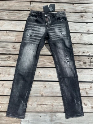 Dsquared2 jeans slim fit  - Säljer ett par svarta skinny jeans med slitningar och blekta detaljer. Jeansen har fem fickor, knappgylf och coola distressed effekter framtill och baktill. Materialet är denim med stretch för skön passform. Perfekta för en trendig streetwear-look.