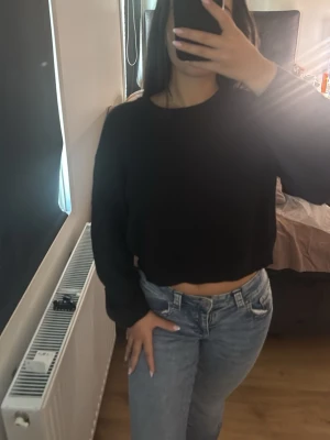 Svart cropped stickad tröja - Säljer en svart, ribbstickad cropped tröja med långa ärmar. Tröjan har en enkel och stilren design som passar perfekt till jeans eller kjol. Materialet är mjukt och stretchigt för en bekväm känsla. Perfekt för lager på lager under kyligare dagar.