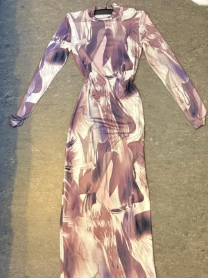 Långärmad abstrakt klänning Shein - Säljer en långärmad klänning från Shein i abstrakt mönster med lila, beige och vita toner. Klänningen är lång och har en kroppsnära passform med rund hals. Perfekt för dig som gillar unika prints och vill sticka ut.