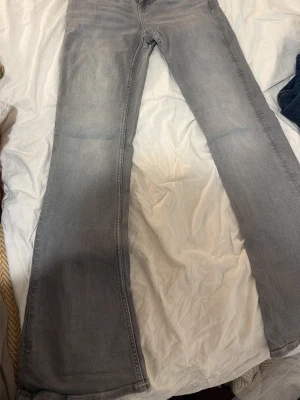 gråa bootcut jeans  - Säljer ett par gråa bootcut jeans med lätt slitning på låren. Jeansen har klassisk femficksdesign och är tillverkade i denim med lite stretch för skön passform. Perfekta för dig som gillar en avslappnad men ändå trendig look.