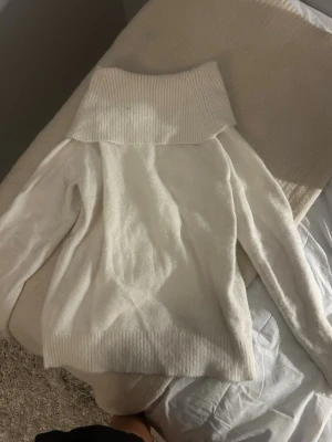 Vit polotröja i stickat material - Mysig vit stickad polotröja med bred, ribbad krage och långa ärmar. Tröjan har en avslappnad passform och ribbade muddar vid ärmslut och nederkant. Perfekt för kalla dagar och enkel att styla till olika outfits. Aldrig använd och köpt för 400 kr