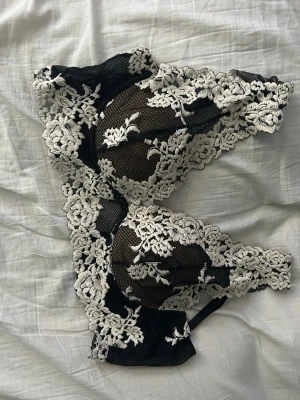 Intimissimi bh - Säljer en elegant svart Intimissimi bh med vacker vit spetsbrodyr. Bh:n har mjuka kupor utan vaddering och breda spetsband som ger en romantisk look. Materialet är genomskinligt mesh med detaljerad blommig spets. Perfekt för dig som gillar feminina underkläder.