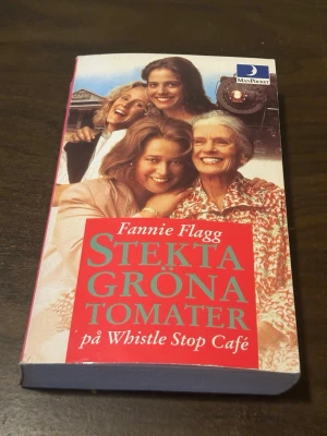 Stekta gröna tomater pocketbok - Säljer romanen 'Stekta gröna tomater på Whistle Stop Café' av Fannie Flagg. Pocketbok med färgstarkt omslag som visar fyra kvinnor och ett tåg i bakgrunden. Boken är på svenska och utgiven av ManPocket.