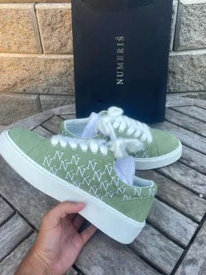  skor - Snygga gröna sneakers med vit sula och vita skosnören. Skorna har ett mönster av vita N-loggor på sidorna och är tillverkade i mockaliknande material. Perfekta för dig som vill ha en clean och trendig look. Sitter som 44. De är för stora för mig, jag har 43.