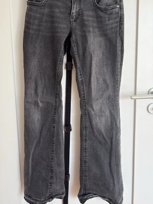 Mörkgråa bootcut jeans med detalj på bakfickan  - Jag säljer ett par mörkgråa bootcut jeans med knappar på bakfickorna. Jeansen har klassisk femficksmodell, dragkedja och knapp i midjan samt snygg tvättad look. Perfekta för en avslappnad outfit. Jeansen är i storlek 42 och är ifrån ginatricot. Säljs då det inte är i min storlek längre. Jeansen är en aning slitna längst ner vid foten. 
