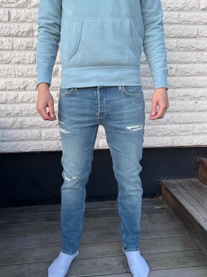 Ljusblå slitna slim fit jeans - Säljer ett par ljusblå slim fit jeans med slitningar på låren och knäna. Jeansen har klassisk femficksdesign och normal midja. Materialet är denim i bomull och passformen är smal hela vägen ner. Perfekta för en avslappnad och trendig look. Storlek 30/30