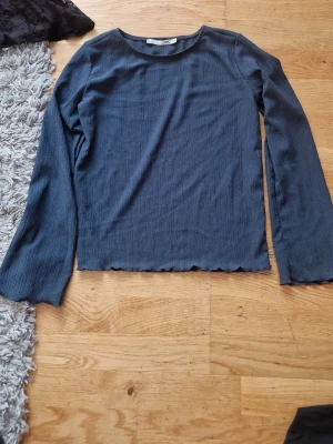 Mörkblå ribbad långärmad topp - En enkel och stilren mörkblå ribbad topp med långa ärmar. Toppen har en rak passform och lätt vågig kant nedtill för en avslappnad look. Perfekt att matcha med jeans eller kjol.