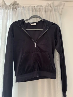 Marinblå Juicy Couture kofta - Mjuk och skön svart hoodie i velour med dragkedja framtill och känguruficka. Tröjan har huva och långa ärmar, perfekt för en avslappnad och trendig look. Passar till både jeans och mjukisbyxor. Jätte fint skick, har även ett par marinblå Juicy byxor om någon är intresserad i XXS. Storlek 12/13 men skulle säga att den passar xxs 