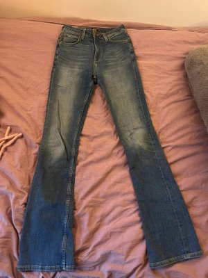 Blå bootcut jeans från Lee - Snygga blå bootcut jeans från Lee med klassisk femficksdesign och lätt slitning på låren. Jeansen har normalhög midja och utsvängda ben, perfekta för en avslappnad och trendig look. Tillverkade i denim med en skön passform.