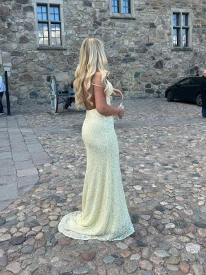 Lång glittrig balklänning från dressroom - Säljer en lång gul klänning/balklänning  med v-ringning och figurnära passform. Klänningen är täckt av glittriga paljetter och har smala axelband. Modell Lumi från Dressroom Göteborg S färg Lemon. Jag är 170cm lång.