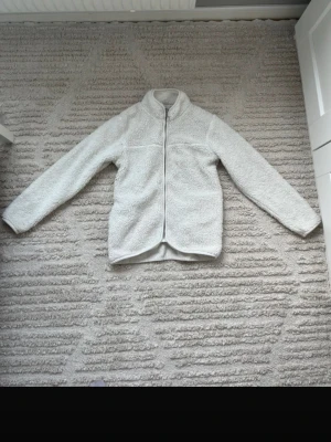 Vit teddyjacka med dragkedja - Supermjuk och fluffig vit teddyjacka med hel dragkedja framtill och hög krage. Jackan har en enkel, stilren design och ger en mysig känsla och trendig look.