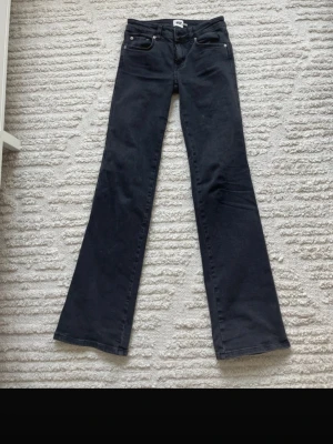 Svarta bootcut jeans - Snygga svarta bootcut jeans med klassisk femficksdesign och utsvängda ben. Jeansen har silverfärgade nitar och knappdetaljer. Perfekta för dig som vill ha en tidlös och trendig look.
