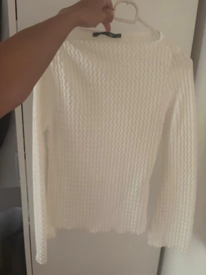 Vit ribbstickad tröja - Säljer en vit ribbstickad tröja med lång ärm och rund hals. Tröjan har ett snyggt strukturmönster och är gjord i ett mjukt material som känns skönt mot huden. Perfekt att matcha med jeans eller kjol för en clean look.