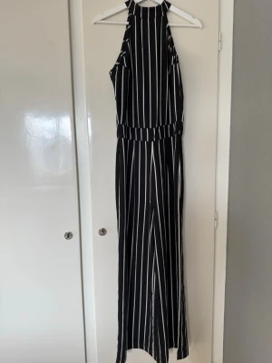 Svartvit randig jumpsuit med halterneck - Snygg svart jumpsuit med vita vertikala ränder och halterneck. Vida ben och markerad midja ger en trendig siluett. Sminkrester jag ej försökt få bort. Köpt via här tidigare, aldrig använd av mig då den är för stor & lång för mig. Jag väger 49kg & är 164cm för info. 