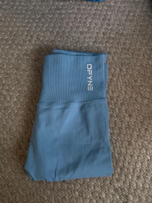 Blå seamless leggings från DFYNE - Snygga blå seamless leggings från DFYNE med hög midja och ribbad linning. Materialet är stretchigt och mjukt, perfekt för träning eller chill. Scrunch-detalj bak för extra passform och stil. Logga framtill i vitt. (Aldrig använd)