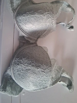Ljusgrå spets-bh med vaddering - Snygg ljusgrå bh med vadderade kupor och vacker spetsdetalj över hela bh:n. Justerbara axelband och hakknäppning bak. Perfekt för dig som gillar en feminin och stilren look.