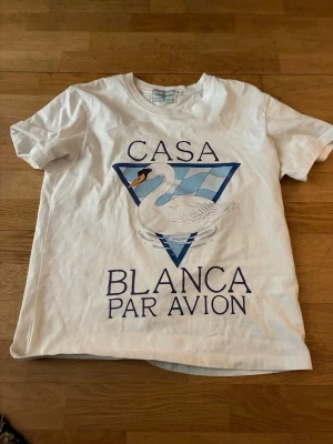 Vit Casa Blanca t-shirt med svanmotiv - Vit t-shirt från Casa Blanca med tryck av en svan och texten 'Casa Blanca Par Avion' på framsidan. Klassisk passform och korta ärmar, perfekt för en avslappnad stil. Tillverkad i mjuk bomull för skön komfort.