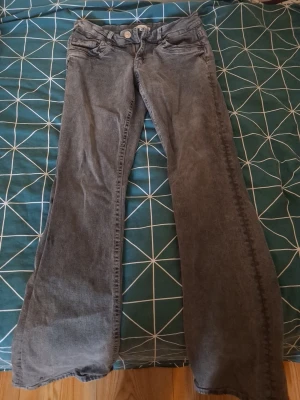 Grå bootcut jeans från Gina Tricot - Säljer ett par grå bootcut jeans från Gina Tricot. Jeansen har klassisk femficksmodell, normal midja och utsvängda ben. Tillverkade i mjukt denimtyg som ger en avslappnad look. Perfekta för dig som gillar retrostil och vill ha något bekvämt.