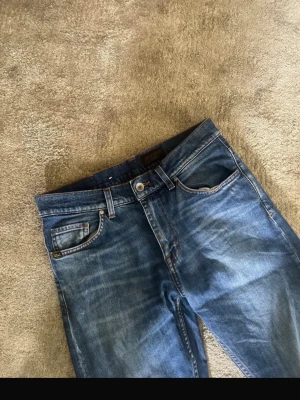 Tiger of Sweden  jeans  - Säljer ett par klassiska blå jeans med raka ben och snygga slitningar på framsidan. Jeansen har fem fickor, bälteshällor och knappgylf. Materialet är denim i bomull och passformen är avslappnad men ändå smal. Säljer pga att jag har växt ur dem