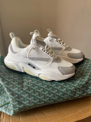 Vita chunky sneakers - Säljer ett par vita chunky sneakers med grå detaljer och meshpaneler. Skorna har en kraftig sula i vitt och beige, samt perforerade partier för extra ventilation. Snygg och modern design som sticker ut.