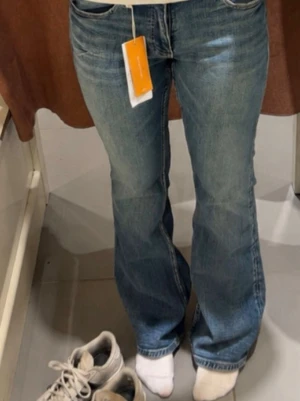 Blå bootcut jeans med broderade fickor - Säljer ett par blå bootcut jeans  broderade detaljer på bakfickorna. Jeansen har klassisk femficksmodell, normal/låg midjade och stängs med två knappar och dragkedja. Köptes på Gina Young för 359 och är i storlek 164 men passar mig som vanligtvis jag S och är ca 162cm Perfekta för dig som gillar en avslappnad men trendig look.