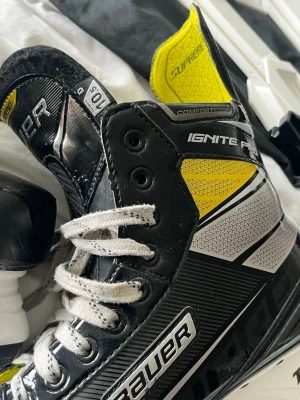 Bauer Supreme Ignite Pro skridskor - Säljer ett par Bauer Supreme Ignite Pro hockeyskridskor i svart, vitt och gult. Skridskorna har vita snören, robust ytterskal och detaljer i silver. Perfekta för isträning eller match. Två extra CCM-skenor medföljer. Stl us 10,5 / (eu 44,5 Använd 2-3 gånger