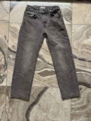 Grå jeans från Lindex - Snygga grå jeans från Lindex i rak modell. Jeansen har klassisk femficksdesign och bälteshällor. Tillverkade i ett mjukt och bekvämt bomullsmaterial med lite stretch för extra komfort. Perfekta för en avslappnad och trendig look.