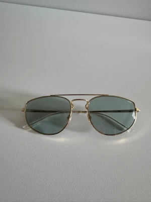 Guldiga Ray-Ban solglasögon - Snygga Ray-Ban solglasögon med tunna guldfärgade metallbågar och gråtonade glas. Klassisk och tidlös design som passar till många olika stilar. 
