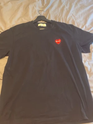 Svart Comme des Garçons PLAY t-shirt - Svart t-shirt från Comme des Garçons PLAY med det ikoniska röda hjärtat med ögon broderat på bröstet. Klassisk rund hals och korta ärmar. Tillverkad i mjuk bomull som känns skön mot huden. Perfekt för en clean och stilren look.