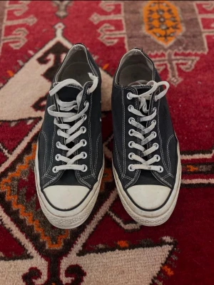 Svarta låga sneakers med vita detaljer - Svarta sneakers med vit sula och vita skosnören. Klassisk låg modell med vita sömmar och tåhätta i gummi. Ovandel i canvas och sula i gummi. Perfekta för en avslappnad och stilren look.