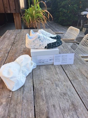 Maison Margiella skor - mörk grön färgstänk  - Unika vita sneakers med grön färgstänk och grön målade tår. Denna model är väldigt efterfrågade men samtidigt väldigt sällsynt att stötta på. Då den är gjord av läder och ovanlig färgstänk. Tillbehör ingår och kvitto finns. Hör av dig vid minsta möjliga fundering!