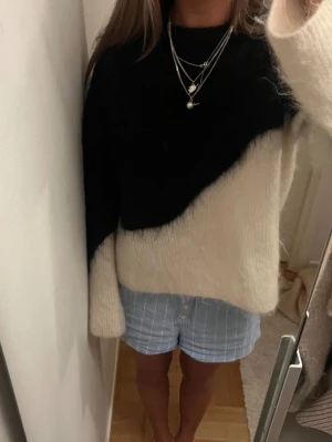 Svartvit fluffig stickad tröja - Säljer en snygg stickad tröja i svart och vitt med diagonal färgdelning. Tröjan är fluffig och har långa ärmar samt rund halsringning. Perfekt för dig som gillar en trendig och mysig look till hösten eller vintern.