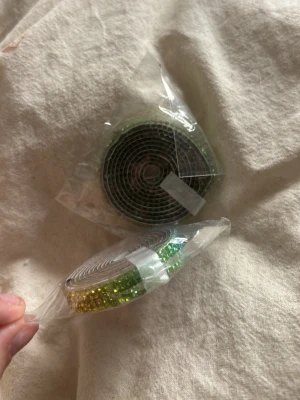 Självhäftande strasstejp i regnbågsfärger - Två rullar självhäftande tejp dekorerade med små glittriga strasstenar i regnbågsfärger och grönt. Perfekt för att pimpa accessoarer, mobilskal eller andra DIY-projekt. Tejpen är flexibel och enkel att använda för att skapa en personlig touch.