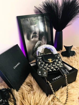 Svart quiltad handväskamed kedja - Snygg svart handväska i quiltat mönster med guldfärgad kedjerem och topphandtag. Väskan har locktängning och en elegant, stilren look som passar till många outfits. Materialet ser ut att vara konstläder och kedjan ger en lyxig känsla.Helt nya .. väldigt elegant ....alla tillbehör medföljer.Har du några frågor är det bara att fråga. Varmt välkommen! 