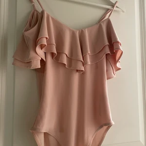 Body storlek XS - En rosa body med volang runt hals och nacke.   Storlek XS - använd ett par gånger. 