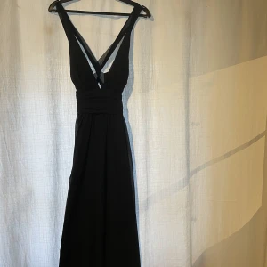 Balklänning - Svart balklänning från Nelly med korsad rygg, v-ringning och vadderade kupor. Använd 1 gång för några år sedan.