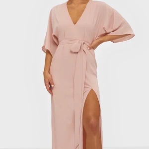 Ljusrosa balklänning - Ljusrosa balklänning med slits framtill, v-ringad och knytning vid midjan (bandet är avtagbart) Helt oanvänd Strl: S/M (Skickar PostNord 66kr, spårbart)