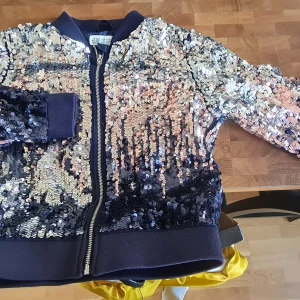 Tröja, paljetter. - Blå paljettjacka, storlek 128. Knappt använd. Knappt synligt slitage på paljetterna, på undersidan av höger ärm, nere vid mudden.