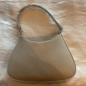 Beige väska - Beige väska, aldrig använd!! Plast och papper kvar innuti. Väskan har ett litet fack på sidan med en dragkedja. Du ka. stänga väskan med den magnetiska knappen. Frakt ingår ej💘