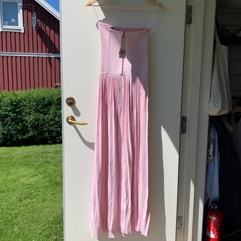 Jättefin rosa klänning med korsetttopp och plisserad kjol. Helt oanvänd med lappar kvar. Köparen står för frakt. . Klänningar.
