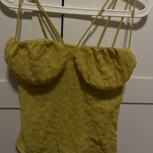 Topp - Gul topp med 4 band, som framhäver brösten. Aldrig använd. Storlek XS. 
