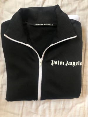 Palm Angels tröja - Långärmad track jacket i svart och vitt från Palm Angels.  Vit ”Palm Angels” logga på bröstet. Ribbstickade muddar i ärmar & krage. Köpt i oktober, använd 2ggr. Kvitto finns, men lapparna är borttagna.  Köptes för 4195kr Storlek: M Material: 100% polyeste