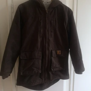 Jacka carhartt - Brun retro jacka från Carhartt. Jackan har huva och är fodrad inuti. Köpt secondhand men har inte kommit till användning.  Står storlek L i jackan men jag är en XS och på mig sitter den perfekt.  Mått: Armhåla till armhåla 51 cm. Längd: 75 cm