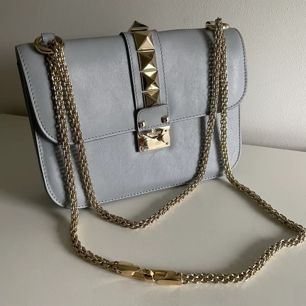Grå handväska med guldiga nitar samt kedja. Kedjan är rörlig så kan användas som axelväska eller handväska. Fake valentino. Väskor.