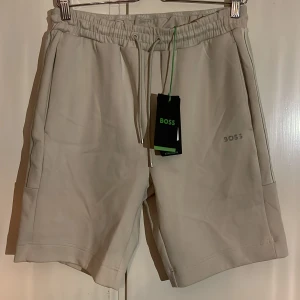 Hugo Boss Shorts - Säljer ett par fräscha och snygga Hugo Boss Shorts i  färgen beige, helt nya med prislappen kvar! Köpta för 1.350kr. Mitt pris är 650kr. På sista bilden kan ni se en ficka på baksidan, den fickan har ett ”ficklock” och är därmed som en kavaj ficka, stängd