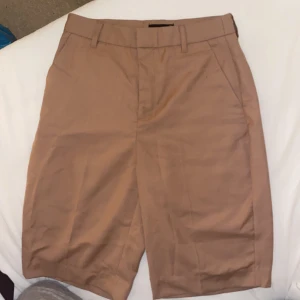Brun kostym lång short från Ginatricot  - En oanvänd brun kostym short som går strax över knäna. Storlek 32-xxs passar som ett xs Ordpris 199kr 
